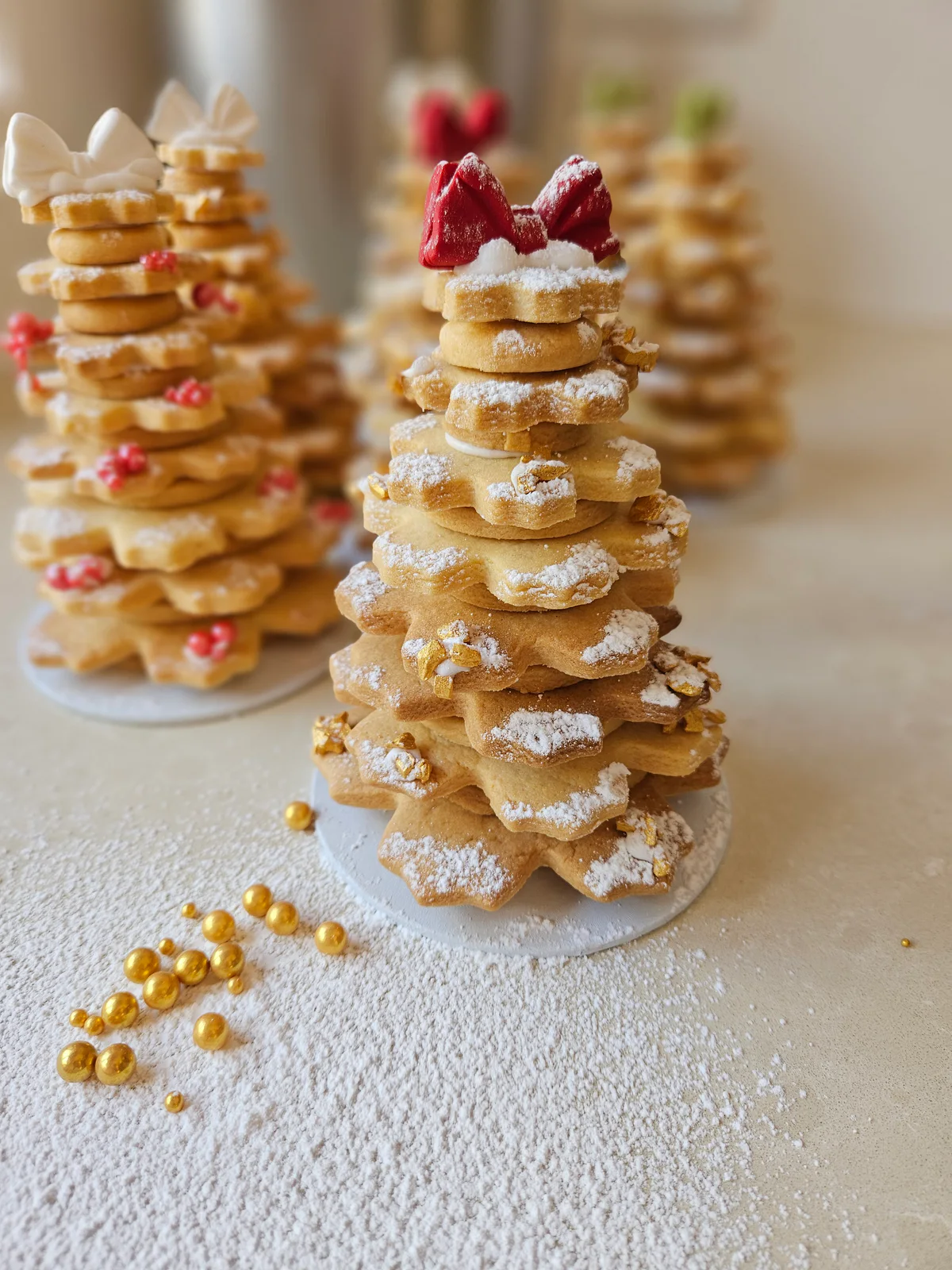 Stacked star-shaped butter biscuit Christmas tree dusted with icing sugar and topped with a red bow, with more biscuit trees behind it.
