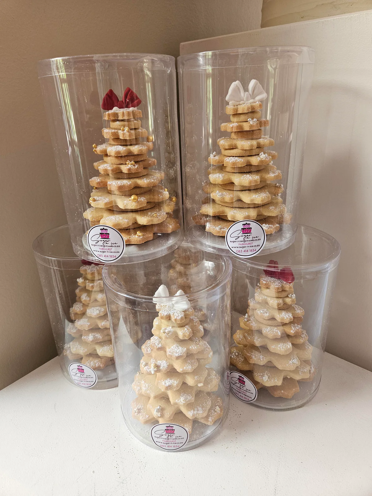 Four butter biscuit Christmas trees with red and white decorations in stacked clear gift tubes.