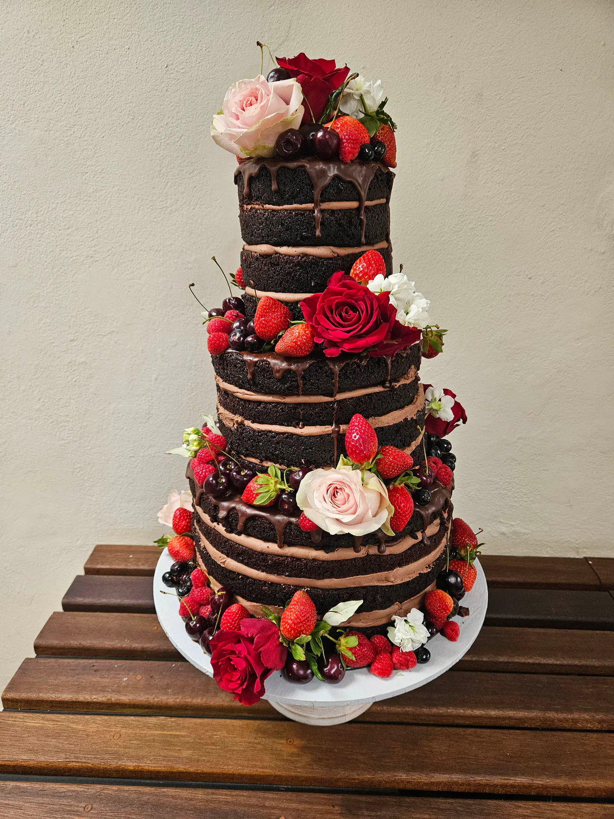 Three-tier exposed-layer chocolate wedding cake decorated with red and pink roses and mixed berries.