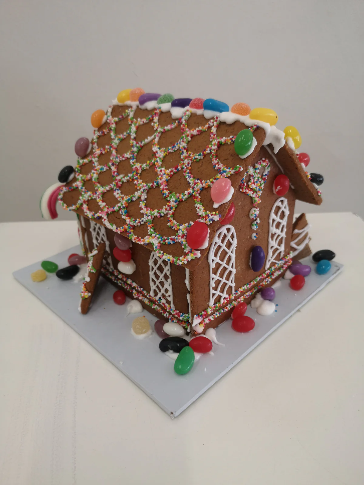 Gingerbread house decorated with white icing, colourful sweets and a lattice-patterned roof.