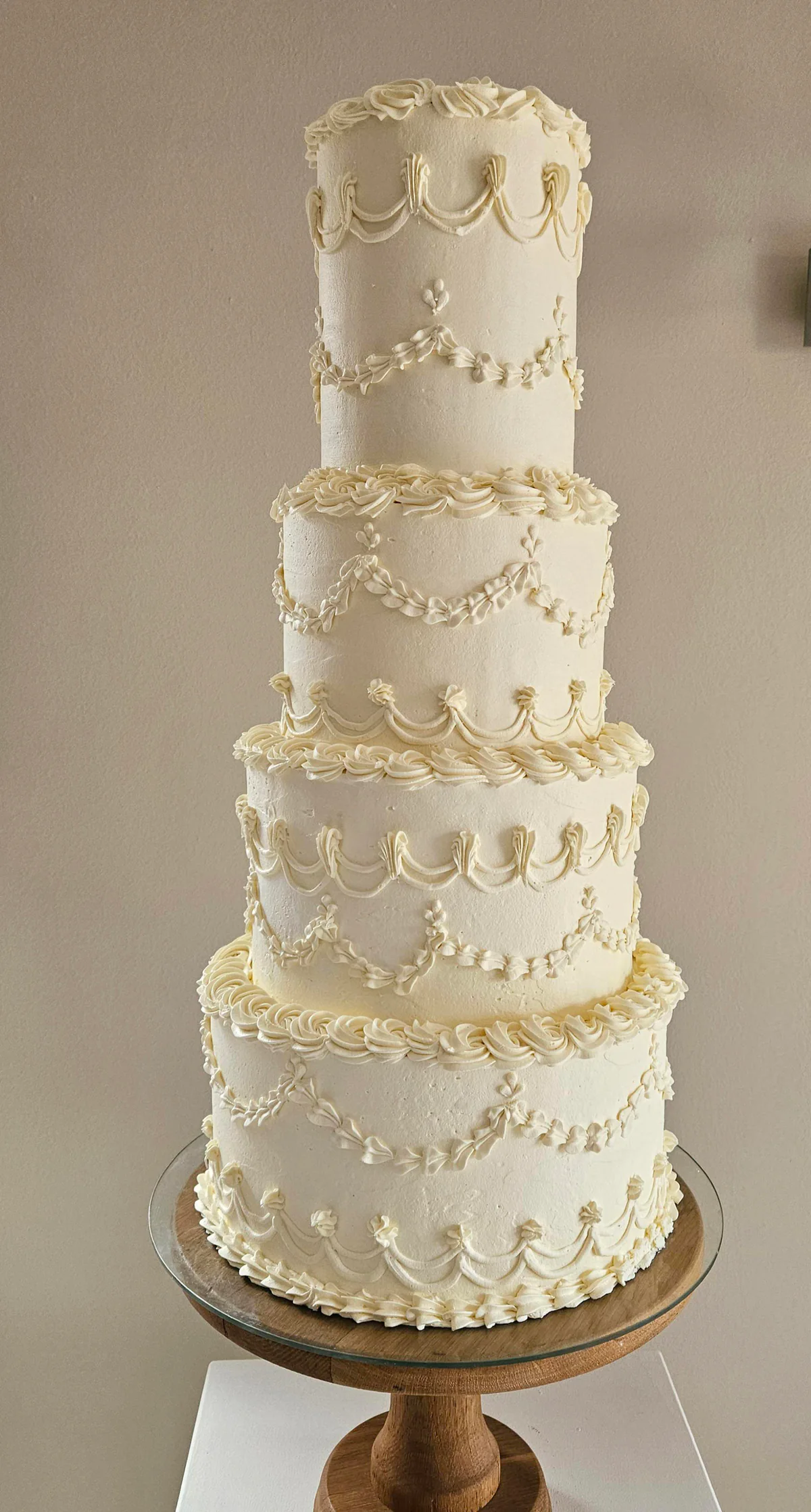 Five-tier ivory wedding cake with ornate piped swags, borders and pearl-like details.