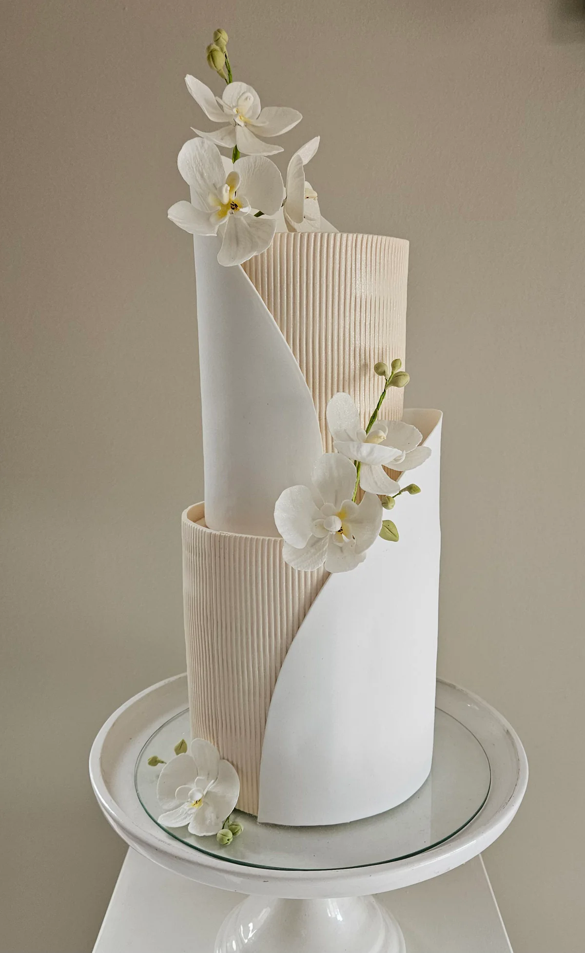 Two-tier white wedding cake with curved ribbed panels and cascading white orchids.