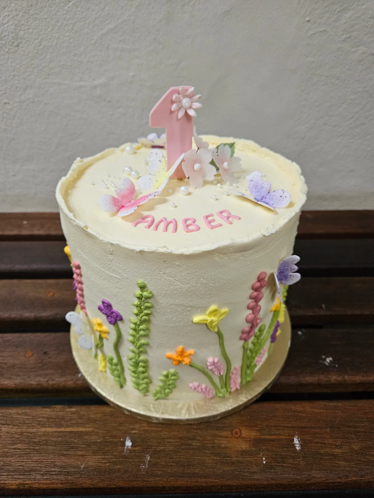 White first birthday cake with pastel piped wildflowers and a pink number one topper.