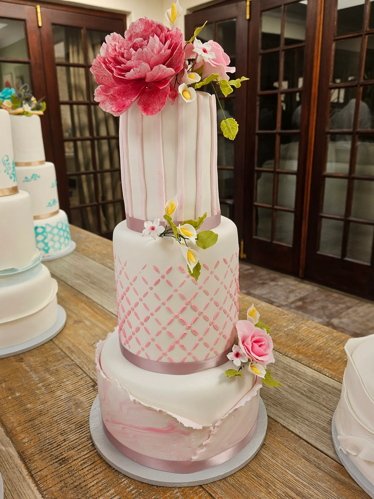 Three-tier pink and white class cake with lattice decoration, marbled details and large pink flowers.