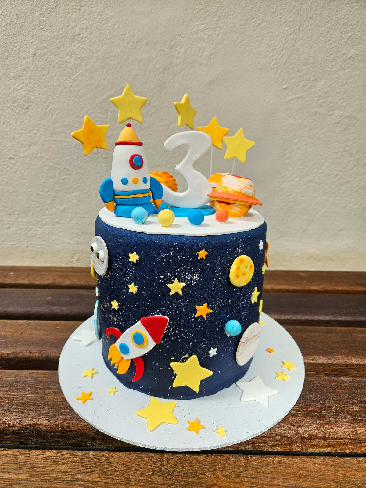 Navy third birthday cake decorated with rockets, planets, yellow stars and a number three topper.